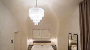 Ein Schlafzimmer mit einem großen Bett, einer Chandelüster, zwei Wandlampen, einem Spiegel und einer Tür zu einem weiteren Raum.