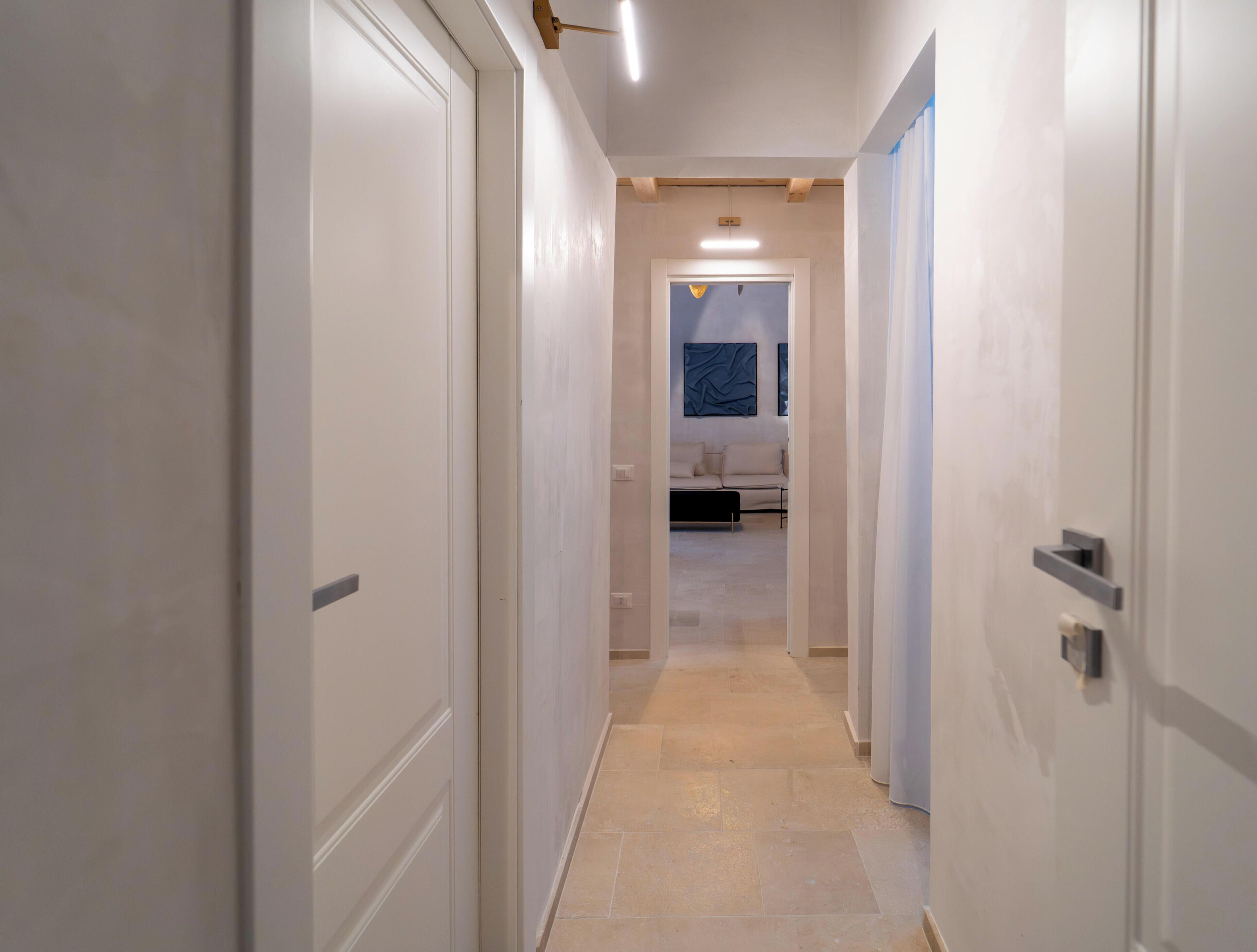 Un couloir avec des portes blanches, un luminaire et un lit au loin.