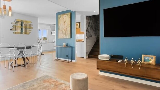 Ein modernes Wohnzimmer mit großem Flachbildfernseher, einem Holz-Nachttisch mit Dekoration und einem Essbereich mit Glastisch und Stühlen.