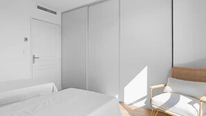 Ein schlicht eingerichtetes Schlafzimmer mit einem Bett, einem Sessel und einem Kleiderschrank.