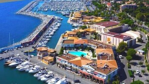 Luftaufnahme einer Marina mit vertäuten Booten, einem Schwimmbad und Gebäuden im mediterranen Stil.