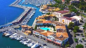 An aerial view of a marina with boats docked, a swimming pool, and buildings with Mediterranean architecture. - Appart Hotel | 3 bedrooms | Parking | swimming pool (Saint Raphaël)
