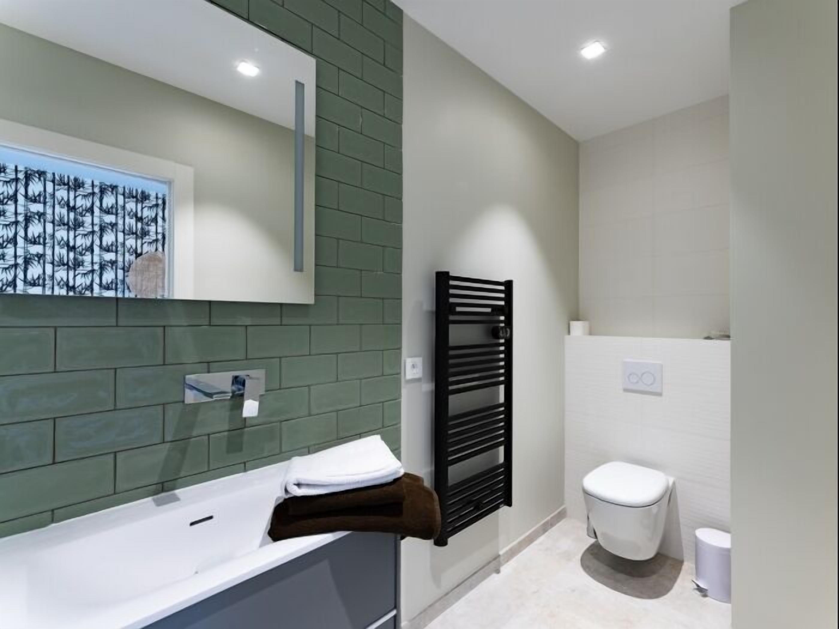 A modern bathroom with a white bathtub, a black towel rack, and a white toilet.