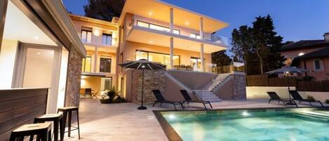 A modern two-story house with a swimming pool, outdoor seating, and a staircase leading to the upper level.