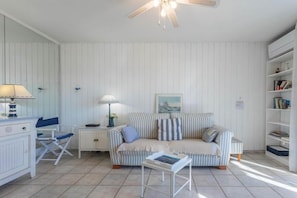 A room with a striped sofa, a small table, a chair, a bookshelf, and a ceiling fan.