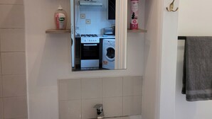 A bathroom with a sink, mirror, towel rack, and a view into the kitchen area. - Charming Luton Apartment Retreat (Luton)
