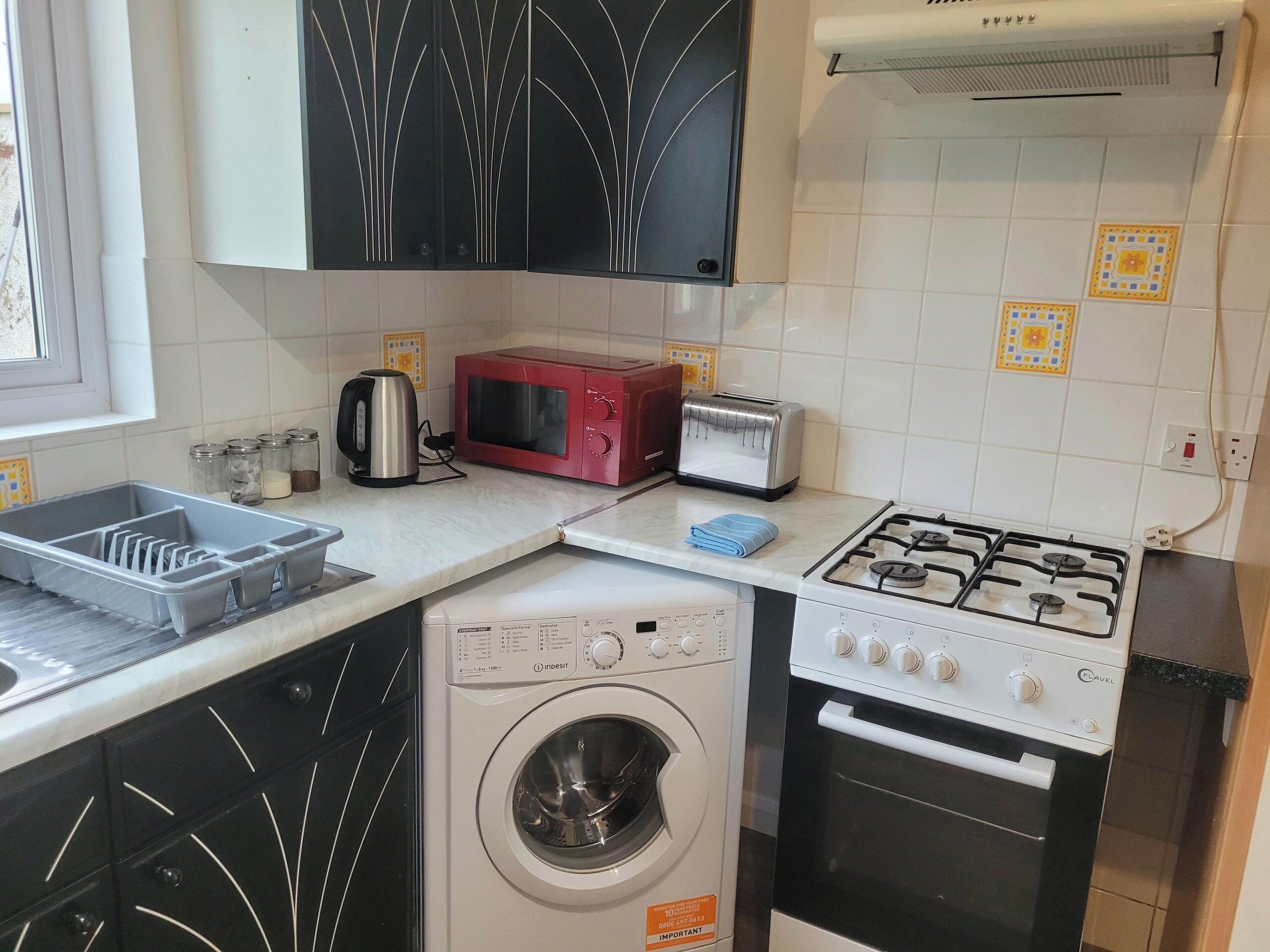 A compact kitchen with a washing machine, a gas stove, a microwave, and a toaster.