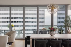 A modern dining area with a white table, black chairs, and a large window with a view of a building.
