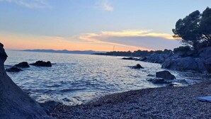 A coastal landscape with rocky terrain, calm sea, and distant mountains.