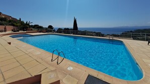 A rectangular swimming pool with a metal ladder, surrounded by tiled flooring, and overlooking a scenic view of the sea and distant mountains.