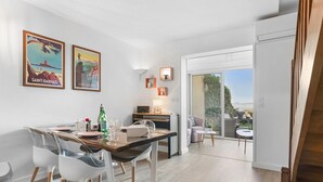 A modern dining area with a wooden table and chairs, a kitchen in the background, and a sliding glass door leading to a balcony with a view.