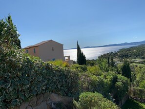 Una casa costera con vista al mar, rodeada de vegetación y colinas.