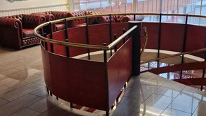 A spacious lobby with a red seating area, a large window with a view, and a ceiling with recessed lighting. - Mehamn Arctic Hotell AS (Gamvik)