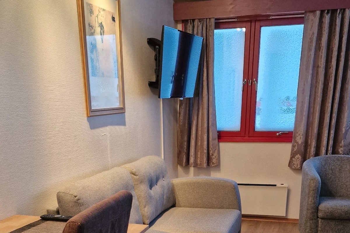 Ein Wohnzimmer mit einer Couch, einem Sessel, einem Tisch und einem an der Wand befestigten Fernseher.