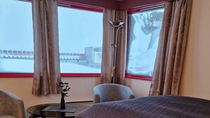 A hotel room with a large bed, a chair, a small table, and a window with curtains. - Mehamn Arctic Hotell AS (Gamvik)