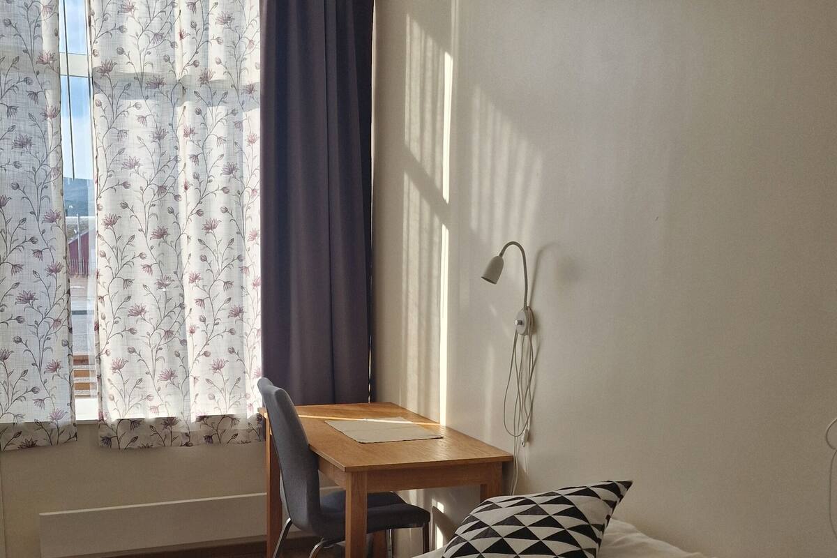 Ein kleiner, gut beleuchteter Raum mit einem Bett, einem Schreibtisch und einem Stuhl.