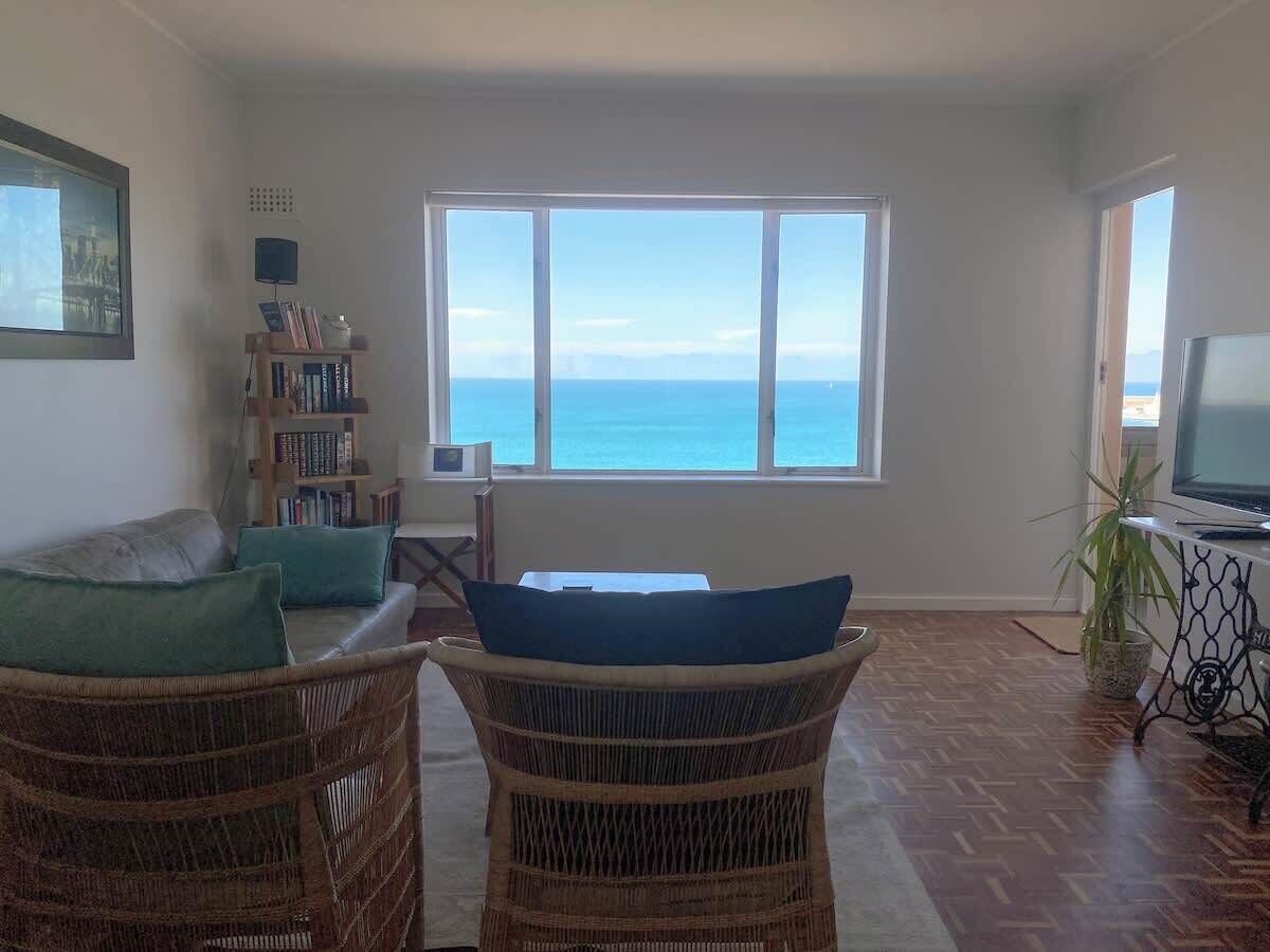 Ein Wohnzimmer mit Meerblick, einem Bücherregal, einem Fernseher und Korbmöbeln.
