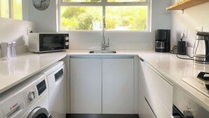 A compact kitchen with a built-in washer and dryer, a microwave, a sink, and a coffee maker. - Simon’s Town Seaside Apt | Views, Balcony, Parking (Cape Town)