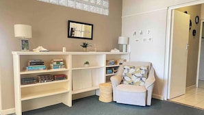 A room with a bookshelf, a chair, and a small table with a lamp. - Sun, Sea & Sand | Beachfront Stay w/ Garage (Cape Town)