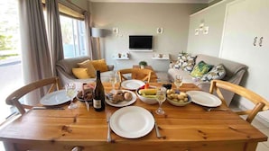A dining area with a wooden table set for a meal, a sofa, and a television in the background. - Sun, Sea & Sand | Beachfront Stay w/ Garage (Cape Town)