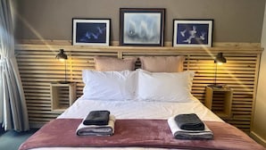 A hotel room with a large bed, two bedside tables, and three framed pictures on the wall. - Sun, Sea & Sand | Beachfront Stay w/ Garage (Cape Town)
