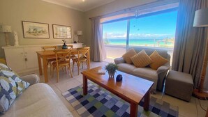 A living room with a view of the ocean, a dining area with a table and chairs, and a sofa. - Sun, Sea & Sand | Beachfront Stay w/ Garage (Cape Town)