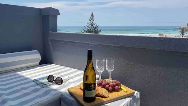 A balcony with a table set for a meal, a bottle of wine, and glasses. - Sun, Sea & Sand | Beachfront Stay w/ Garage (Cape Town)