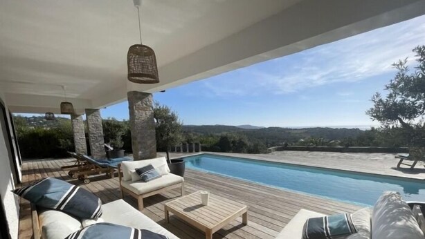 Zona junto a la piscina con terraza de madera, sillas de descanso y vistas al estanque y al paisaje.