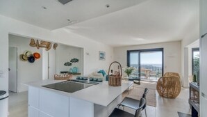 Una cocina moderna con una isla central, armarios blancos y un comedor con sillas negras.