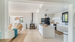 Una cocina moderna con armarios blancos, una isla central y un comedor con mobiliario de mimbre.