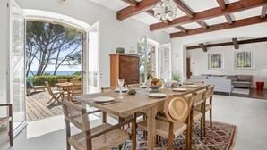 A spacious dining area with a wooden table set for six, surrounded by wicker chairs, a patterned rug, and a view of the sea through an open archway. - Villa 8 pers | waterfront | 180° sea view (.Saint-Raphaël)