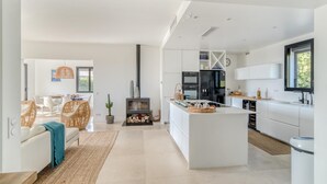 A modern kitchen with white cabinetry, a central island, and a dining area with wicker furniture.