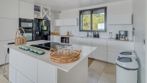 A modern kitchen with white cabinetry, a central island, a built-in oven, and a window with a view of greenery.