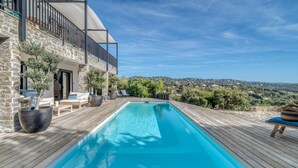 A swimming pool with a wooden deck, outdoor seating, and a view of the countryside.
