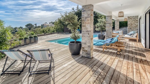A wooden deck with lounge chairs, a pool, and stone pillars.