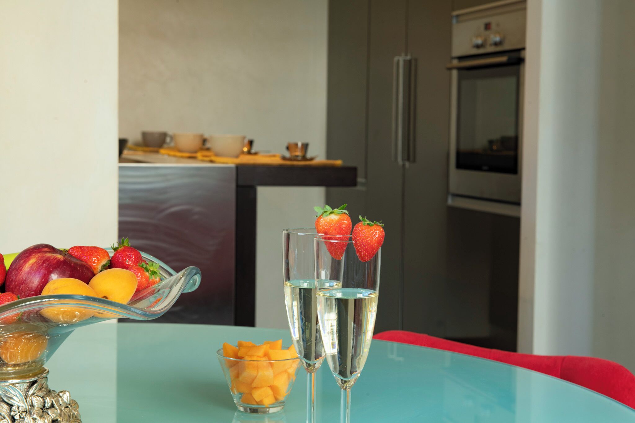 Een tafel met fruit, een glazen schaal en twee glazen met een heldere vloeistof en aardbeien.