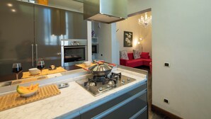Una cocina moderna con estufa a gas, electrodomésticos de acero inoxidable y un sofá rojo en la sala contigua.