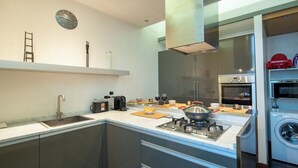 Una cocina moderna con estufa integrada, pileta y lavavajillas. Hay un reloj en la pared y una escalera a la izquierda.