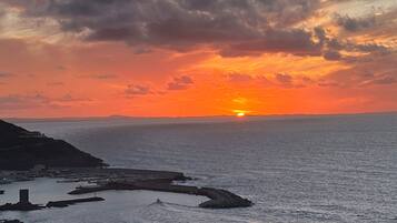 Un coucher de soleil sur la côte, avec une mer calme, une rive rocheuse et des bâtiments situés au loin.