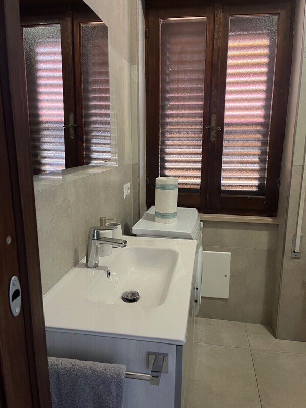 A bathroom with a white sink, a mirror, and two windows with blinds.