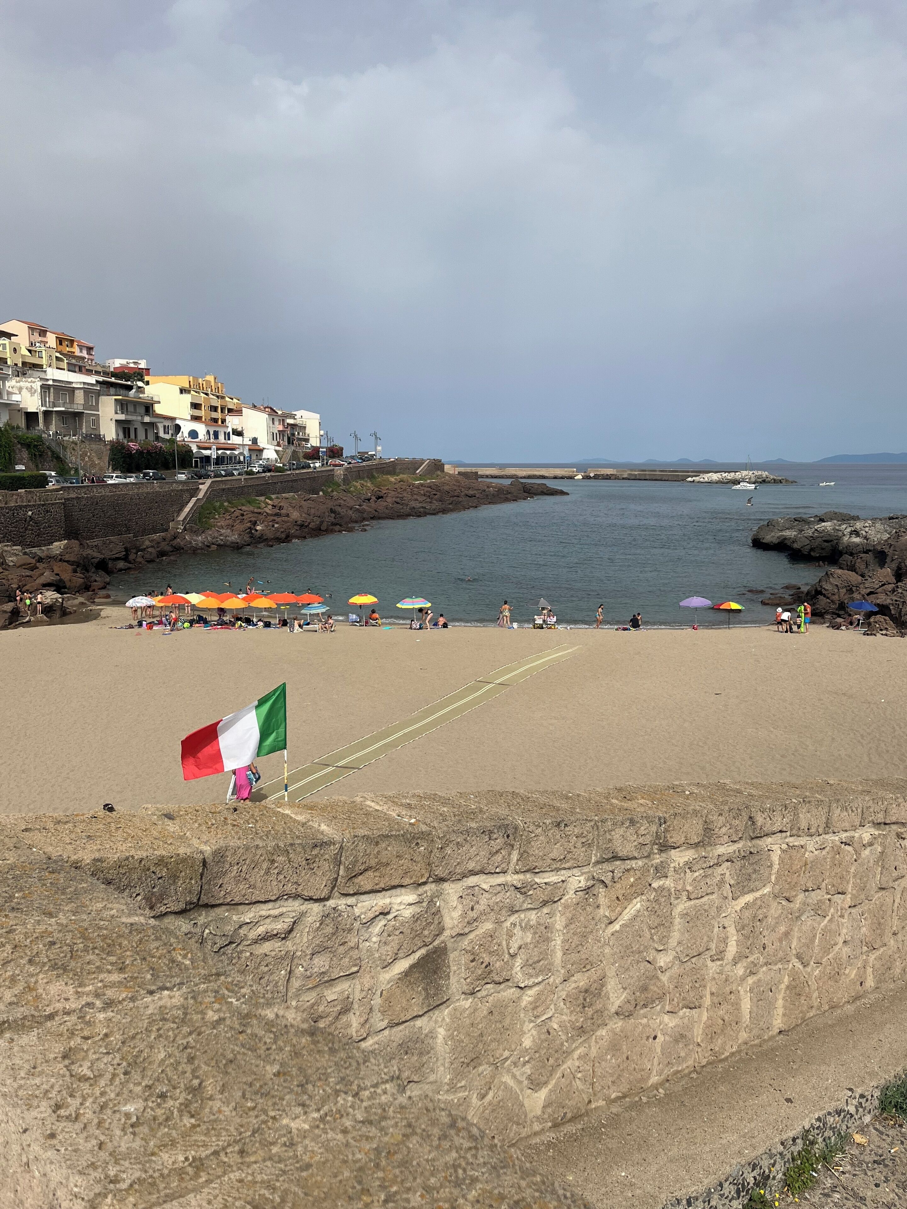 A beach with a flag, umbrellas, and a stone wall.