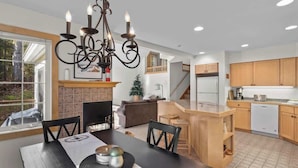 A modern kitchen with wooden cabinets, a built-in island, and a dining area with a black table and chairs.