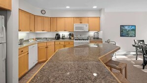 A modern kitchen with wooden cabinets, a granite countertop, a microwave, and a dining area with a table and chairs.
