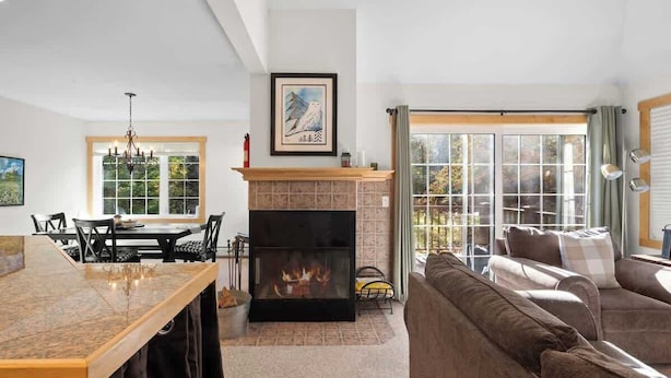 A modern living room with a fireplace, a dining area with a table and chairs, and a large window with curtains.