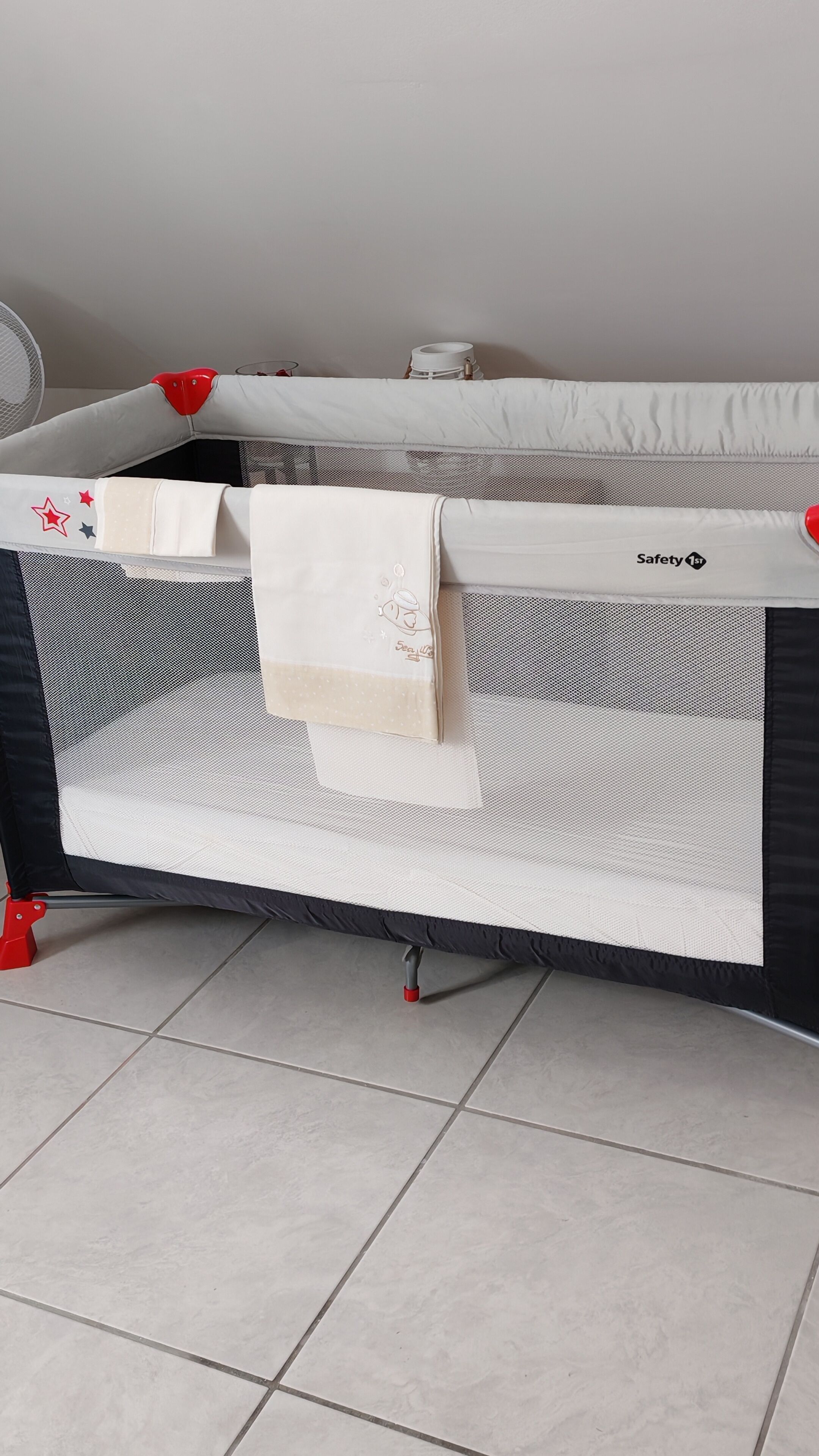 A baby playpen with a safety net, a white cloth, and a red safety strap.
