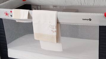 A baby playpen with a safety net, a white cloth, and a red safety strap.