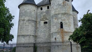 Un château de pierre historique, doté de trois tours, avec une clôture en métal noir au premier plan et une pelouse devant.