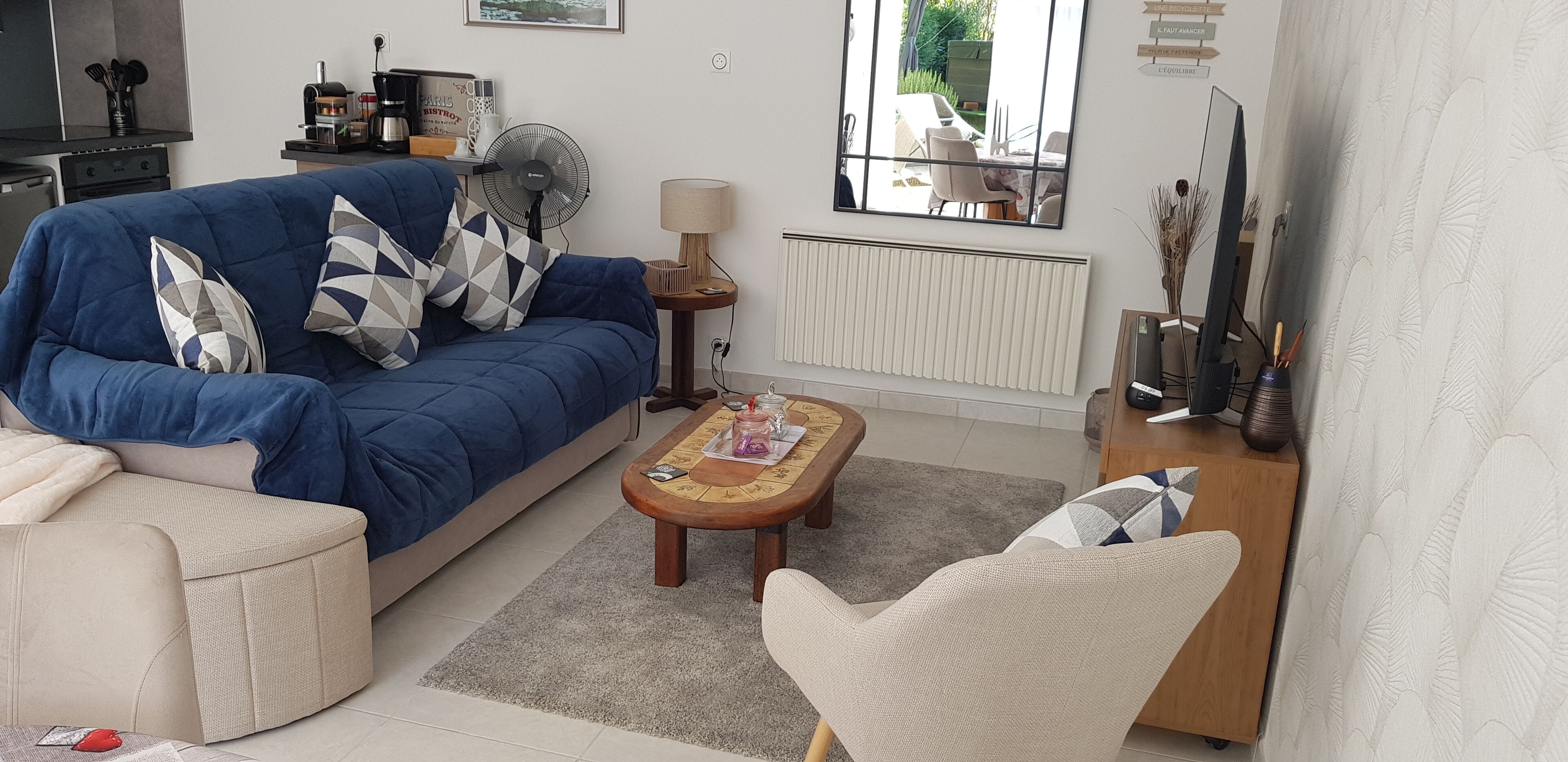 Un salon avec un canapé bleu, une table basse en bois, un fauteuil beige et une petite table d’appoint avec une lampe.