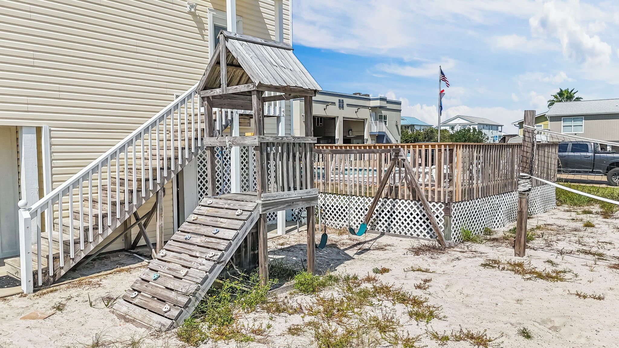Ein Strandhaus mit Holzterrasse, einer kleinen Treppe und einem überdachten Bereich.