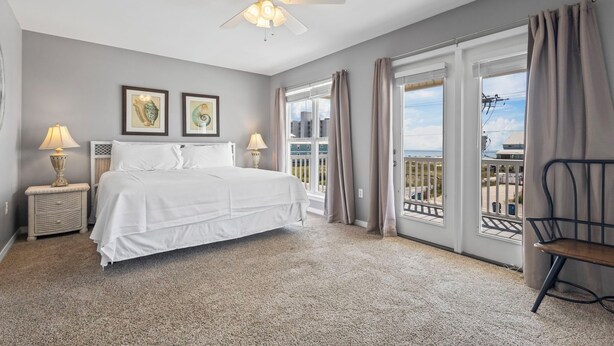 A bedroom with a bed, two bedside lamps, a ceiling fan, and a view of the outside through large windows. - Gulf view retreat w/ Private pool at Summer Salt! (Gulf Shores)
